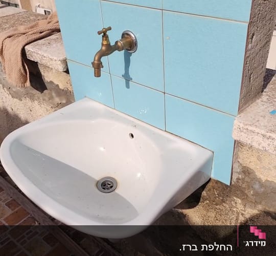 כיור חיצוני עם ברז על קיר מרוצף באריחים כחולים